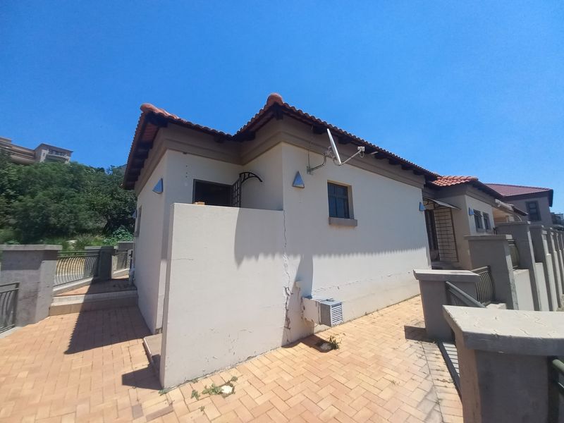 Rear exterior view of the property featuring paved walkways, terracotta roof tiles, and boundary walling with visible structural cracking on the exterior wall.