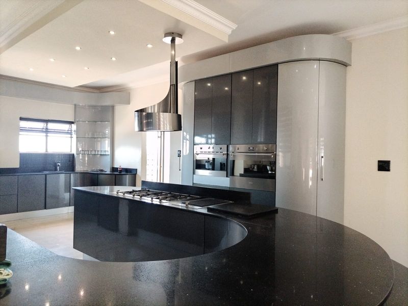Modern kitchen featuring a distinctive curved island with granite countertops, high-gloss cabinetry, built-in double ovens, and a sleek stainless steel extractor hood.