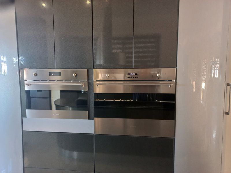 Modern kitchen featuring high-gloss dark cabinetry with integrated stainless steel built-in oven and microwave appliances.