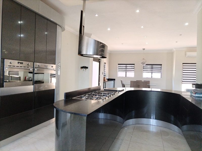 Modern open-plan kitchen featuring a distinctive curved island, high-gloss cabinetry, built-in double ovens, and integrated gas hob, flowing into a bright dining area.