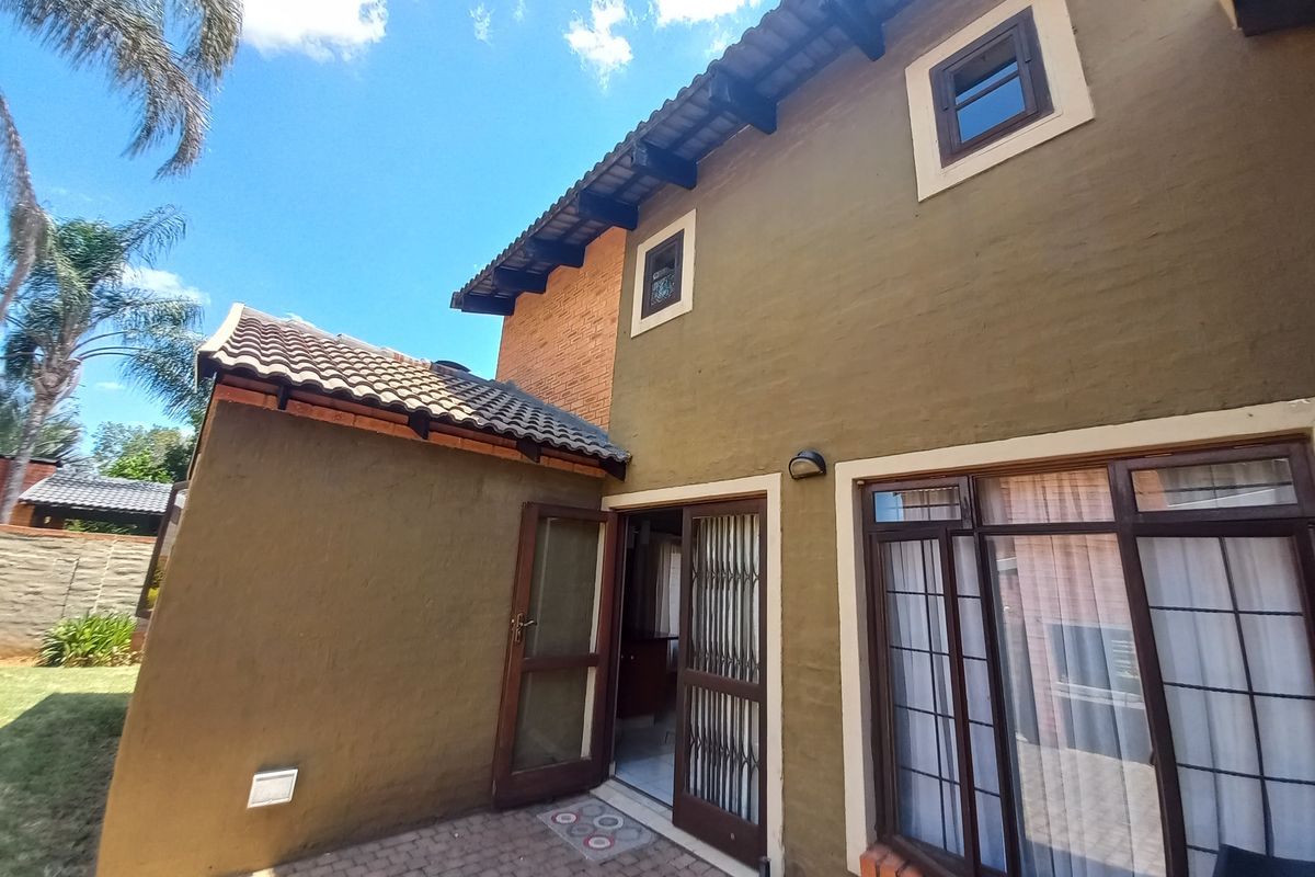 Rear elevation of a two-story house featuring a paved patio area, tiled roof, and security gate access to the interior.