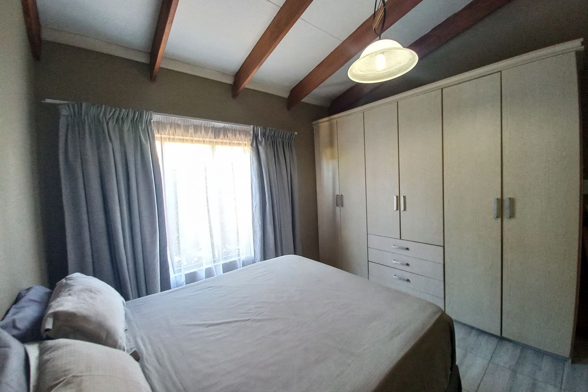 A well-maintained bedroom featuring exposed timber ceiling beams, tiled flooring, and extensive built-in cupboard storage.