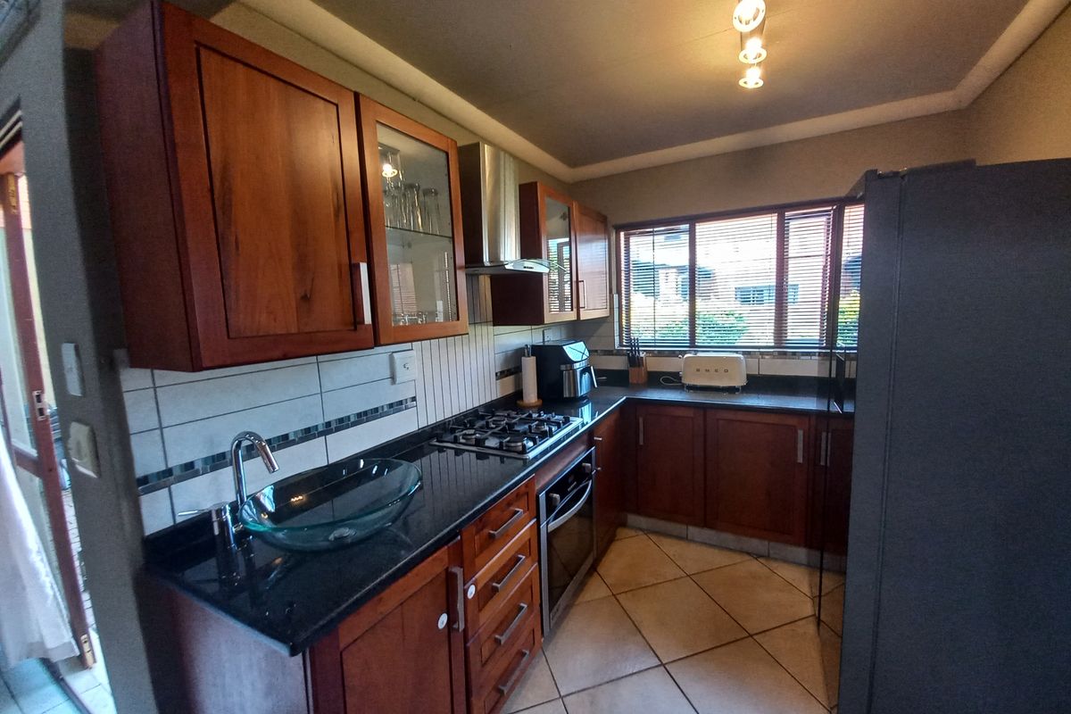 A functional kitchen featuring warm wooden cabinetry, granite countertops, a gas hob, built-in oven, and a unique glass vessel sink.