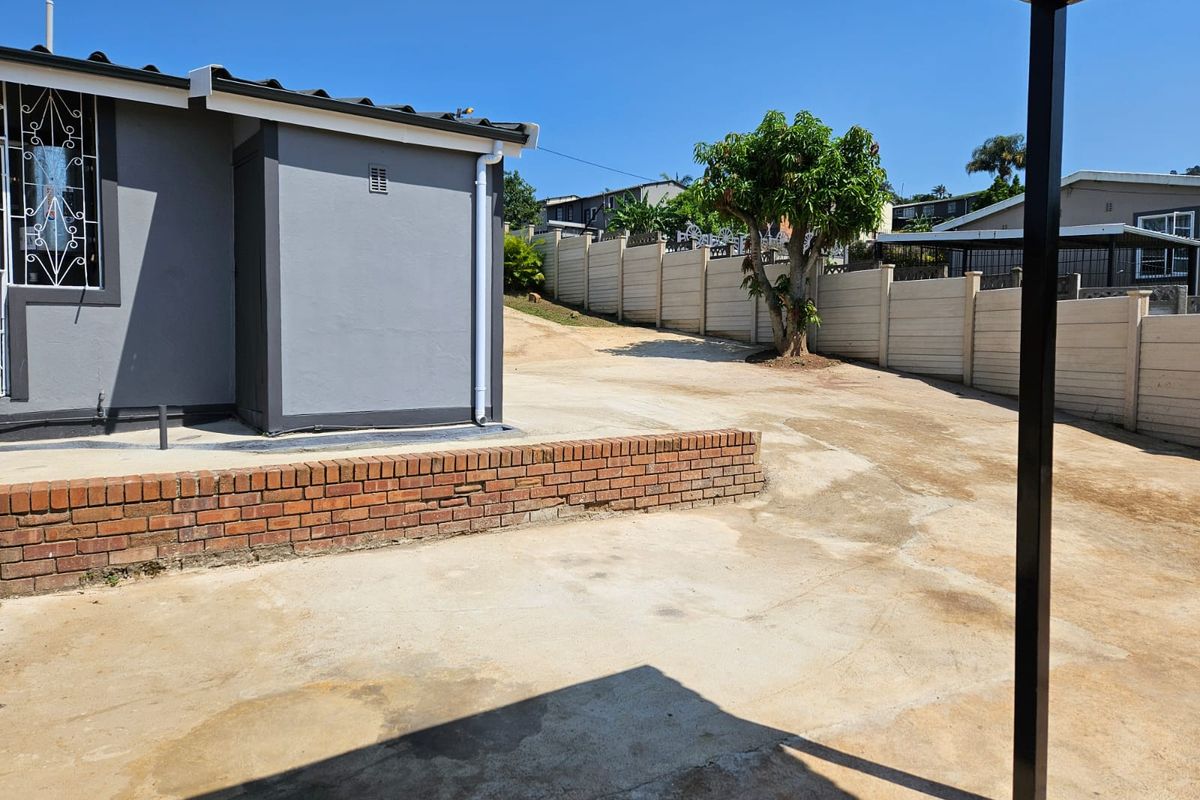 A view of the rear exterior area featuring a concrete driveway, a low brick retaining wall, and perimeter precast concrete walling.