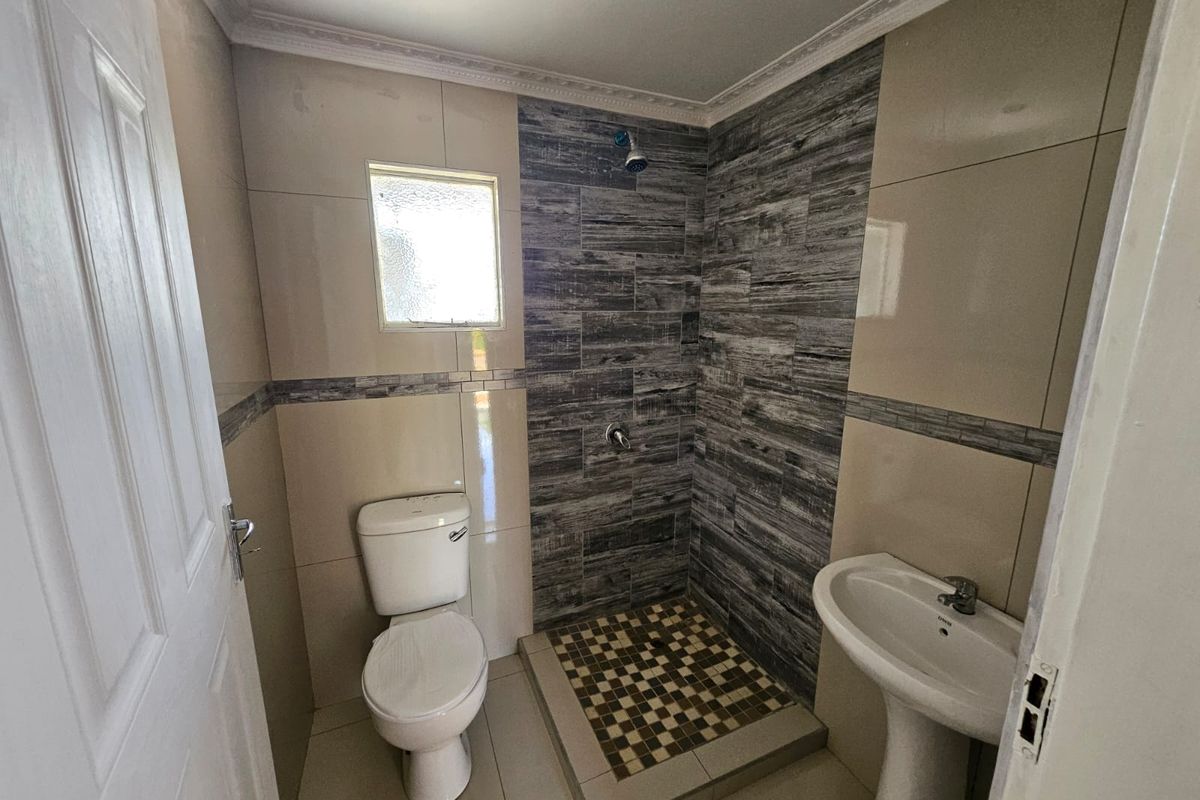 A compact bathroom featuring a walk-in shower with decorative tiling, a pedestal basin, and a standard toilet, finished with modern wall tiles.