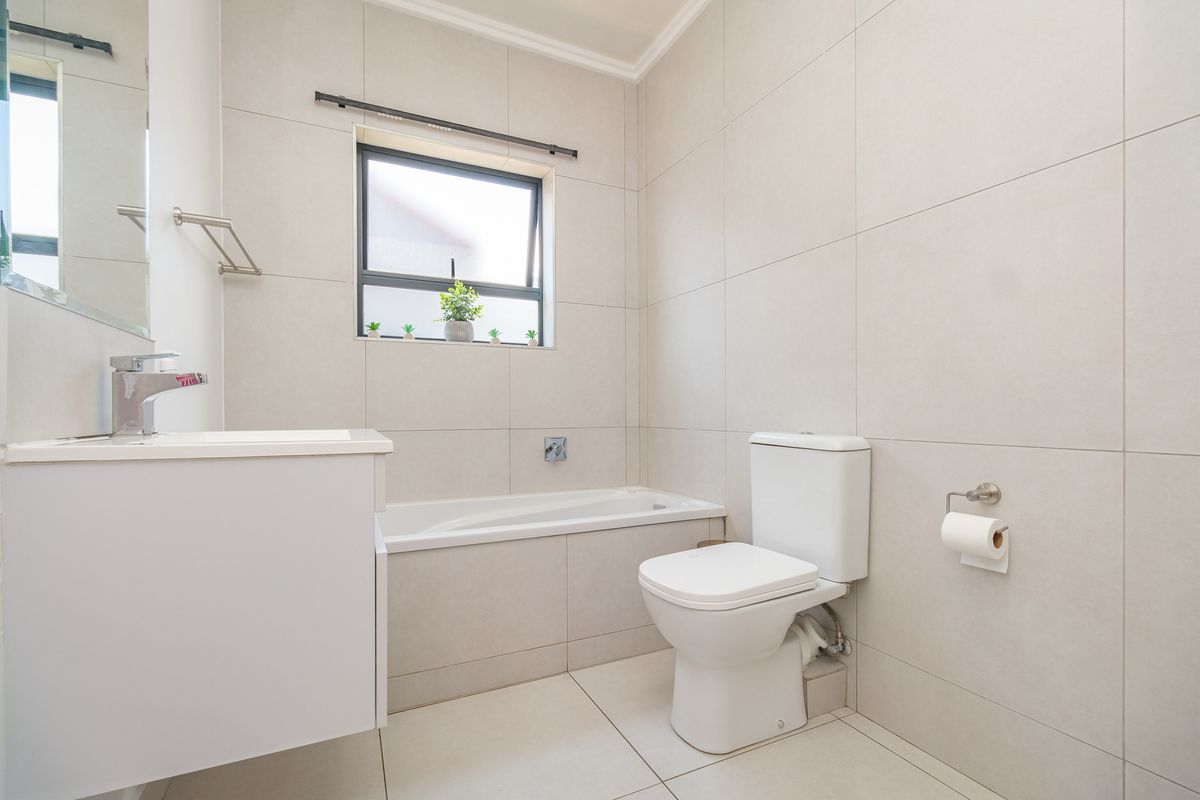 A modern, well-maintained bathroom featuring neutral floor-to-ceiling tiling, a built-in bathtub, a vanity with basin, and a standard toilet.