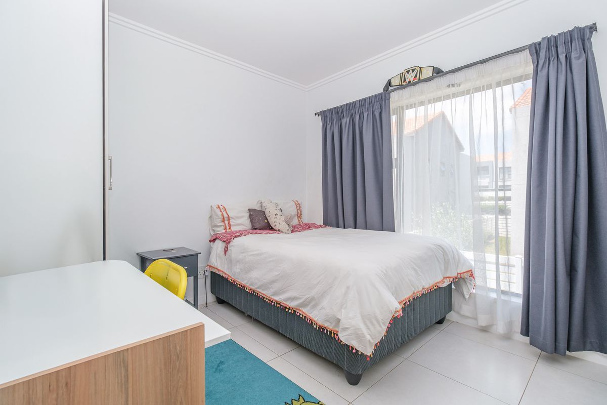 A bright bedroom featuring tiled flooring, a built-in wardrobe, and a large window allowing for ample natural light.
