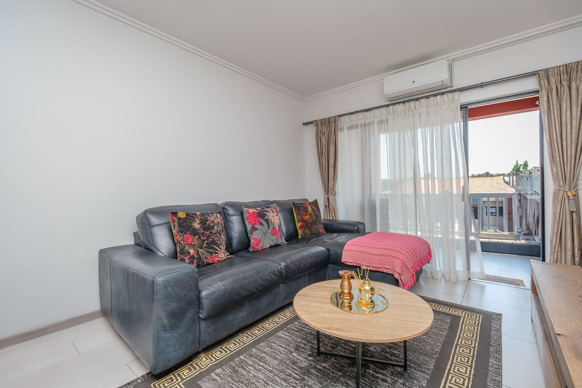 A bright living room featuring tiled flooring, a wall-mounted split-system air conditioner, and direct access to an outdoor balcony through sliding glass doors.