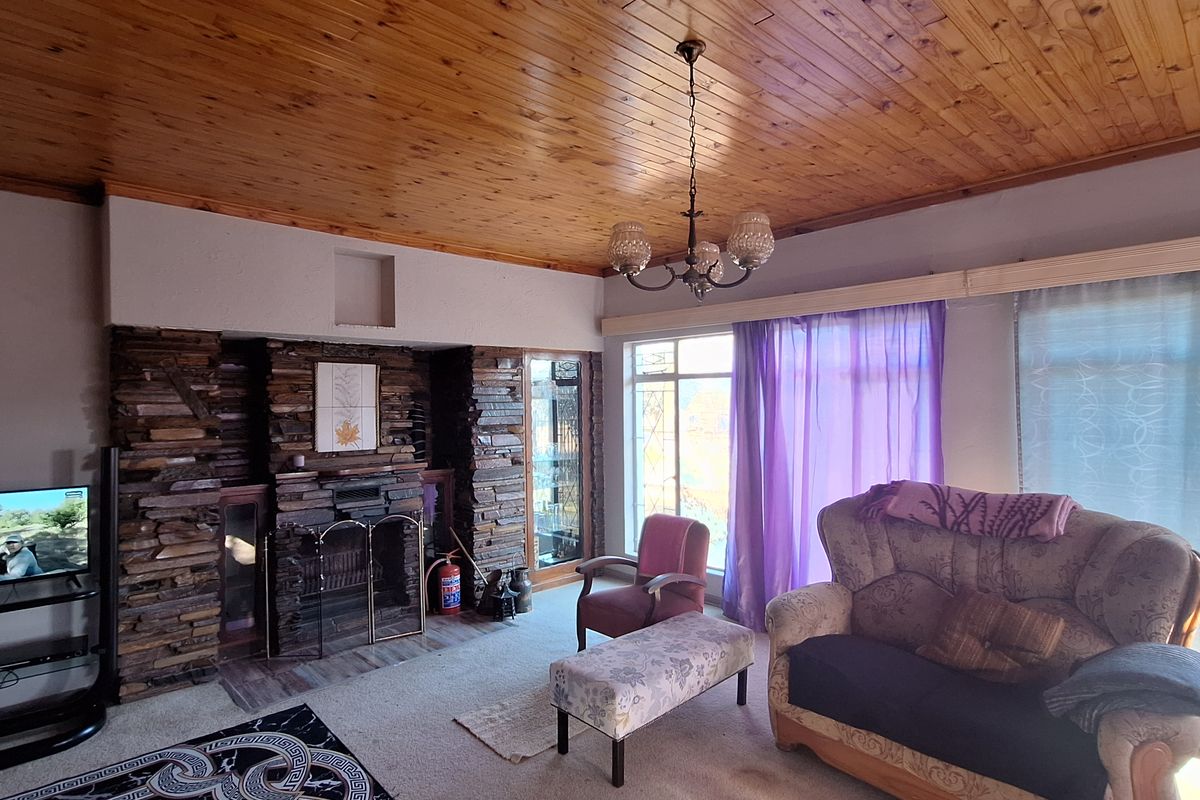 Spacious living room featuring a prominent stone-clad fireplace, large windows with natural light, and a traditional timber-paneled ceiling.