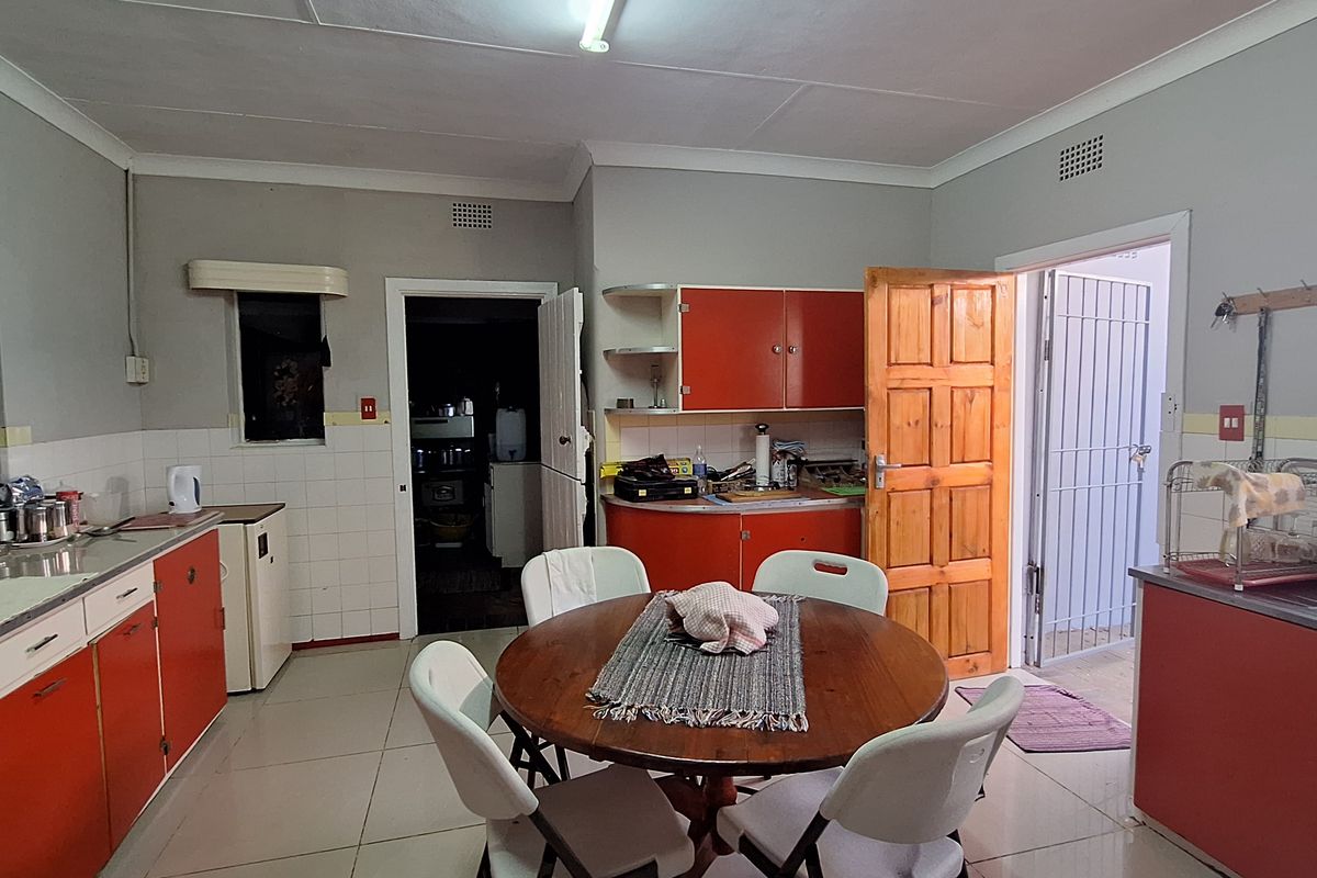 A dated kitchen featuring red cabinetry, tiled splashbacks, and a functional layout with direct access to an adjacent utility area.