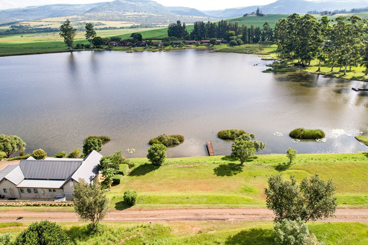 An aerial view of a residential property situated on a large lake, featuring expansive green grounds and scenic mountain views.