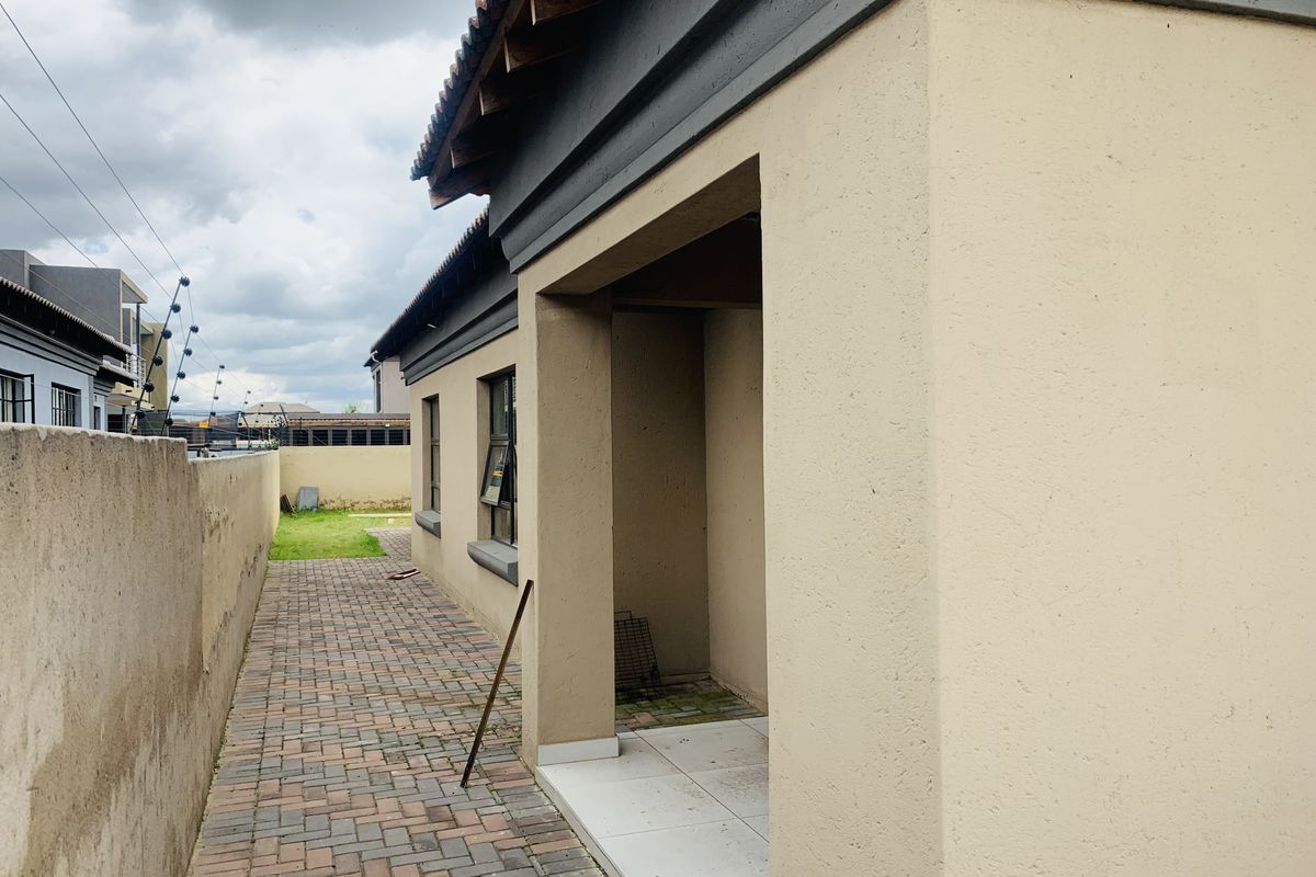 A side view of the property featuring a paved walkway, tiled patio area, and boundary wall with electric fencing.