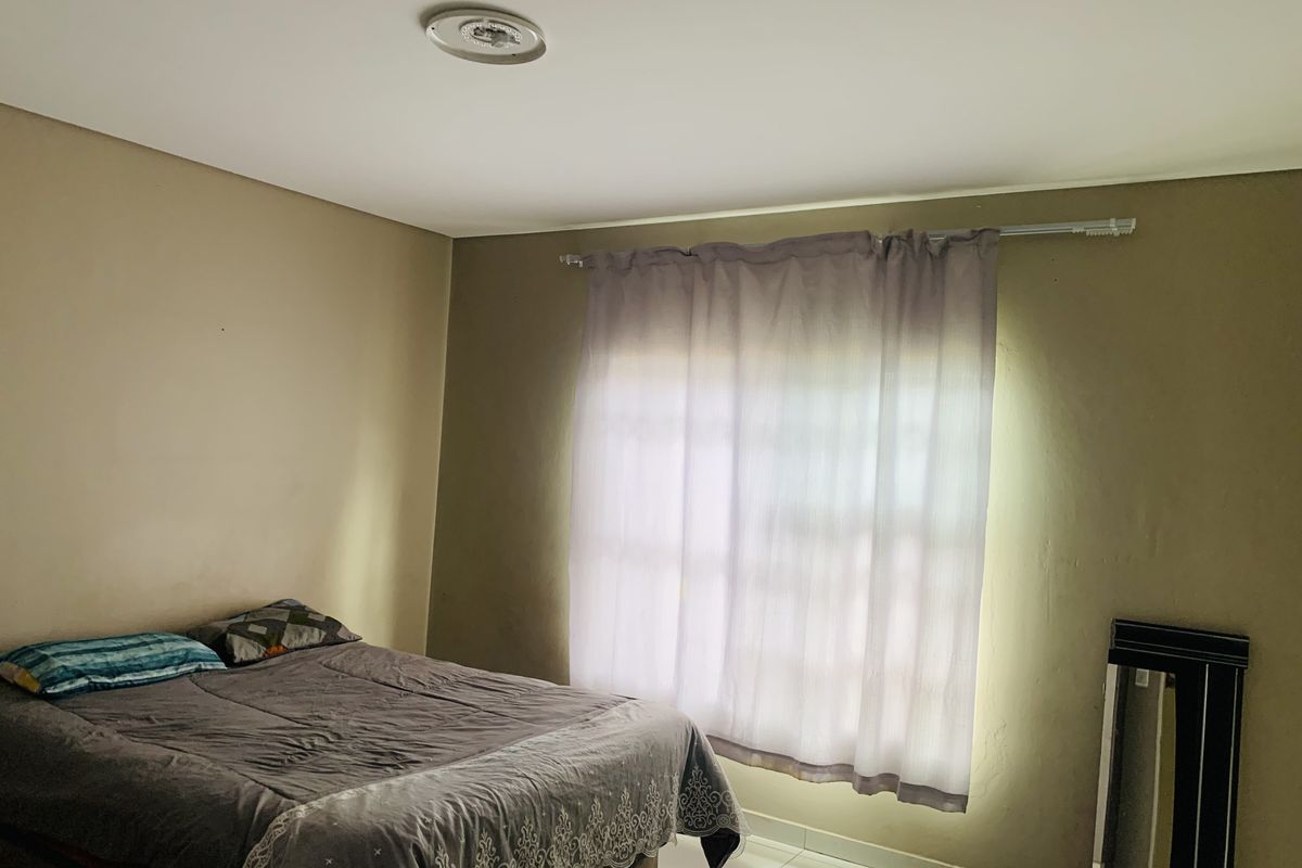 A standard bedroom featuring tiled flooring, neutral wall tones, and a window with installed curtain hardware.