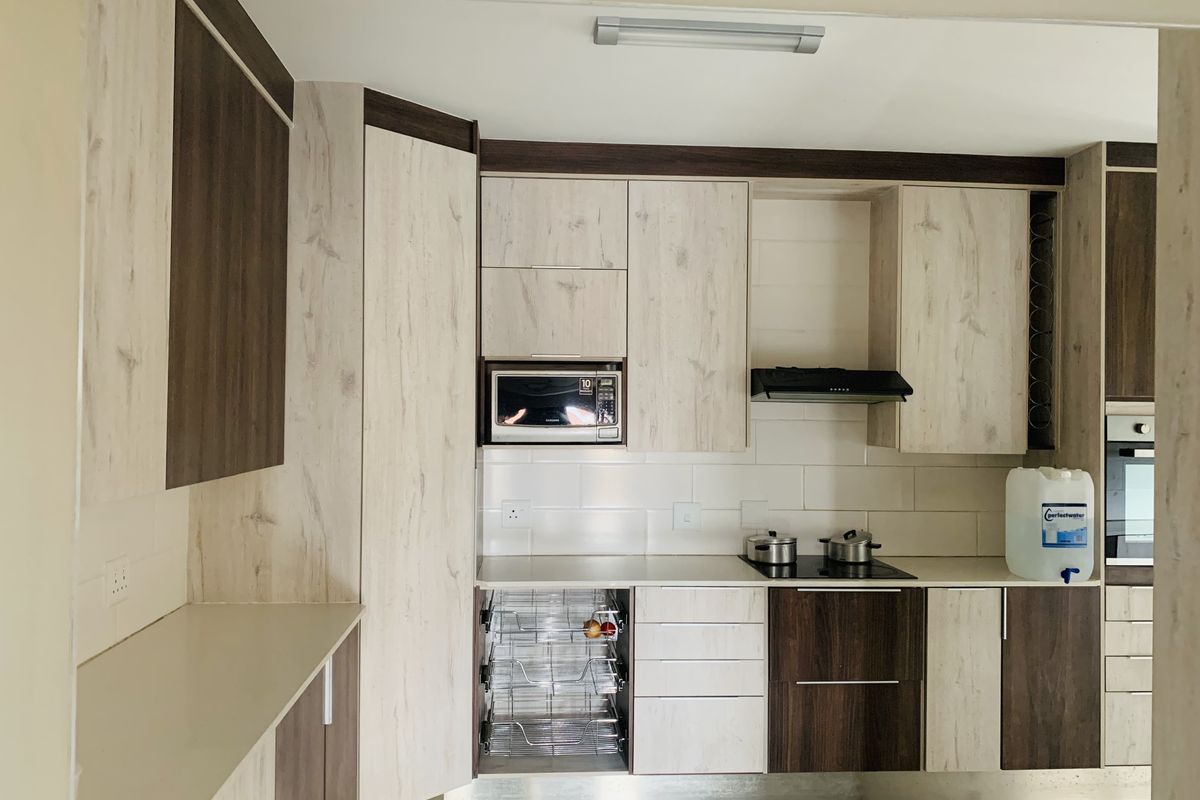 Modern kitchen featuring two-tone wood-grain cabinetry, integrated appliances including a microwave and oven, electric cooktop, and a clean tiled backsplash.