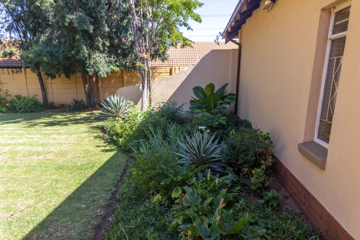 A view of the rear garden area featuring a landscaped garden bed along the side of the house with established plants and lawn.
