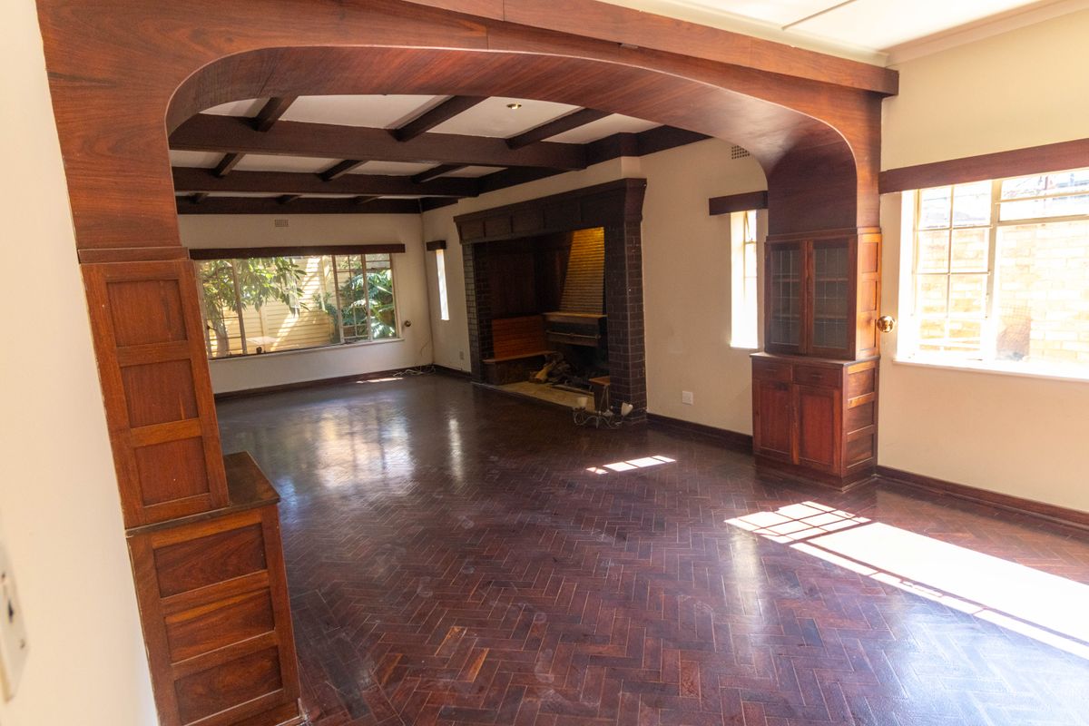 Spacious living room featuring a classic brick fireplace, exposed timber ceiling beams, and original herringbone parquet flooring with built-in wooden cabinetry.