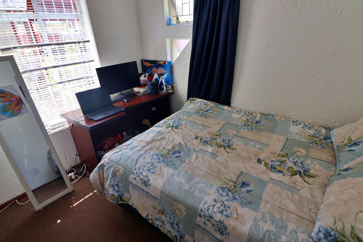 A functional bedroom featuring carpeted flooring, textured walls, and a window with fitted blinds, providing a practical space for rest or study.