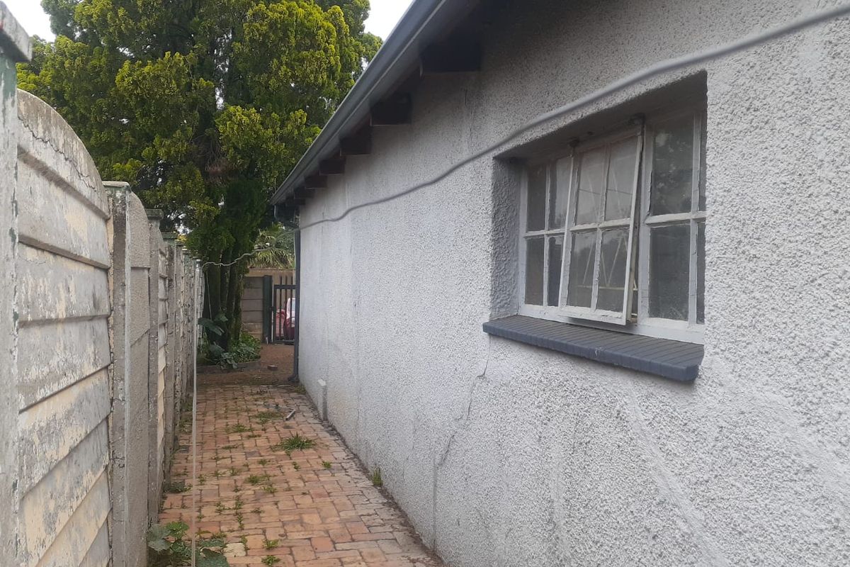 Side exterior view showing a paved pathway, precast boundary wall, and a house wall with visible plaster cracking and a damaged window frame.