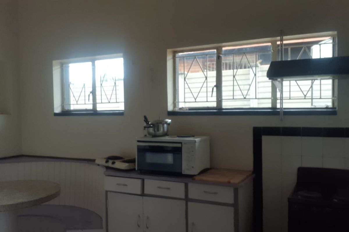 A dated kitchen featuring built-in cabinetry, an extractor fan, and security bars on the windows, offering potential for modernization.