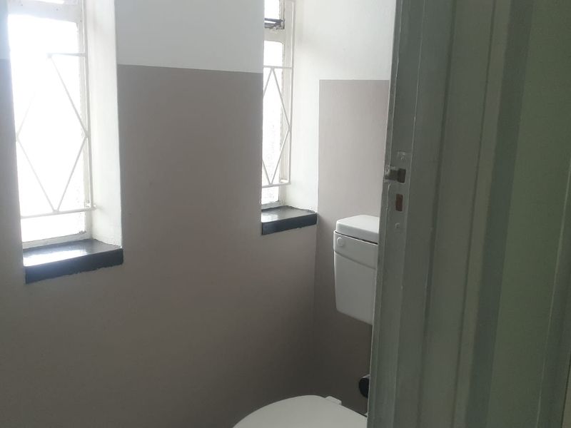 A compact bathroom featuring a standard toilet and two windows with security bars, finished with two-tone wall paint.