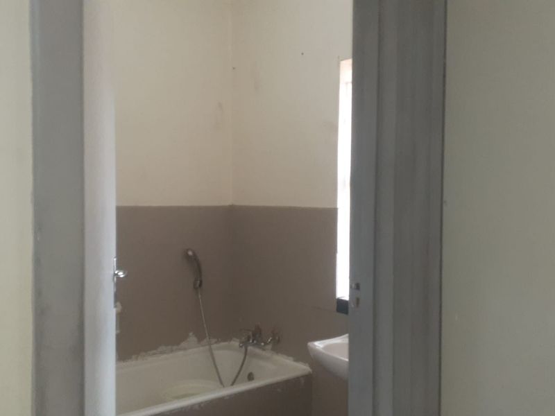 A small, empty bathroom featuring a bathtub with a handheld shower head and a wall-mounted washbasin, currently requiring cosmetic updates and finishing.