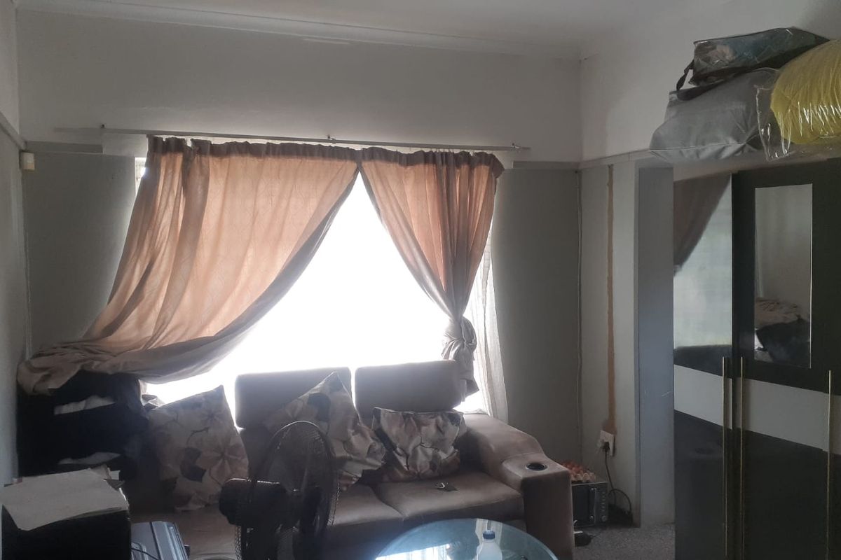 A living room area featuring a large window with curtains and visible wall surface wear, requiring cosmetic attention and maintenance.