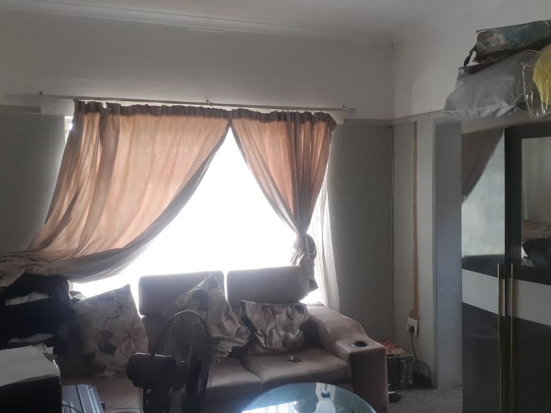 A living room area featuring a large window with curtains and visible wall surface wear, requiring cosmetic attention and maintenance.