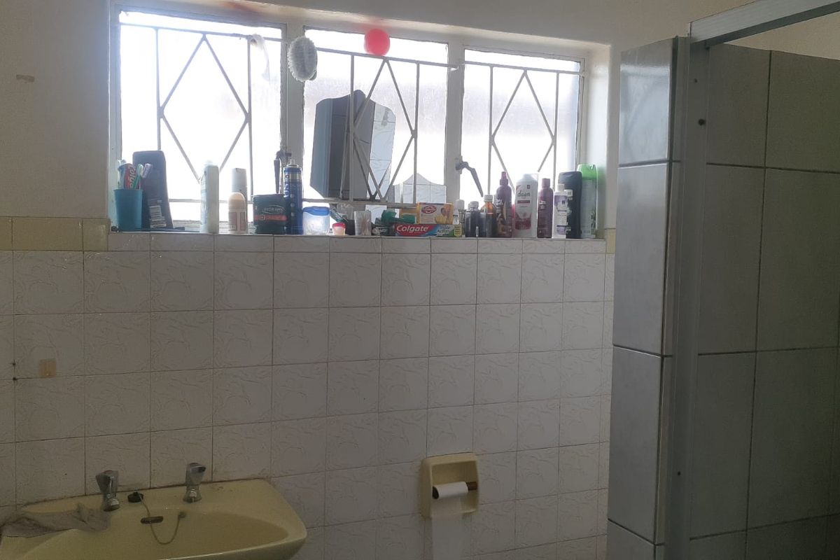 A dated bathroom featuring a pedestal basin, tiled walls, and a shower enclosure, requiring cosmetic updates to modernize the space.