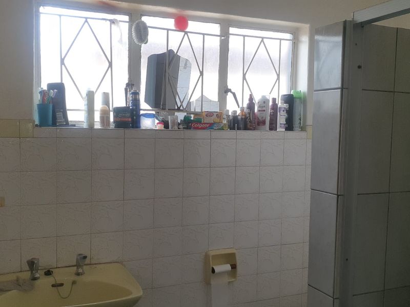 A dated bathroom featuring a pedestal basin, tiled walls, and a shower enclosure, requiring cosmetic updates to modernize the space.