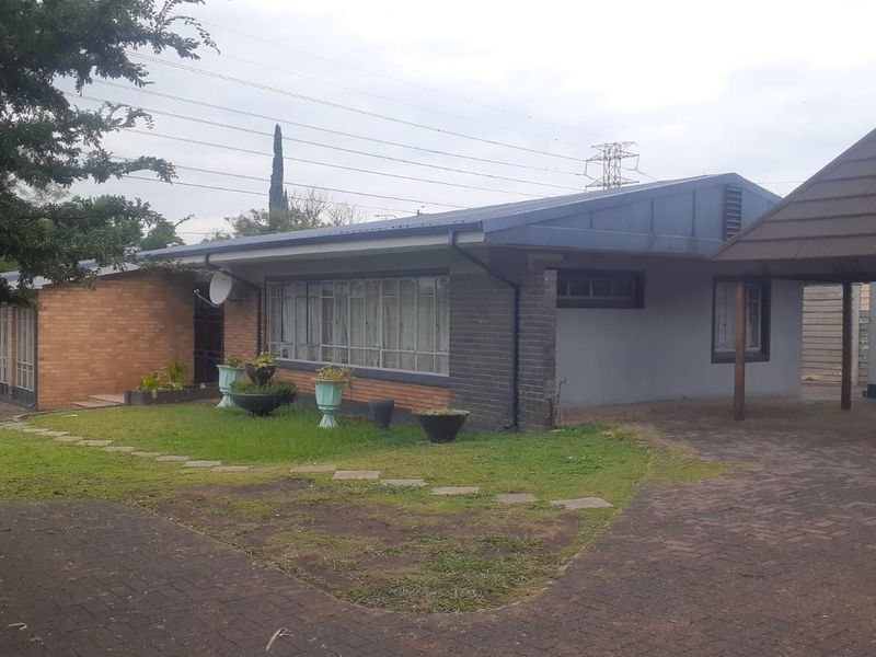 Front exterior view of a single-story house featuring a brick facade, metal roof, and an attached carport with paved driveway.