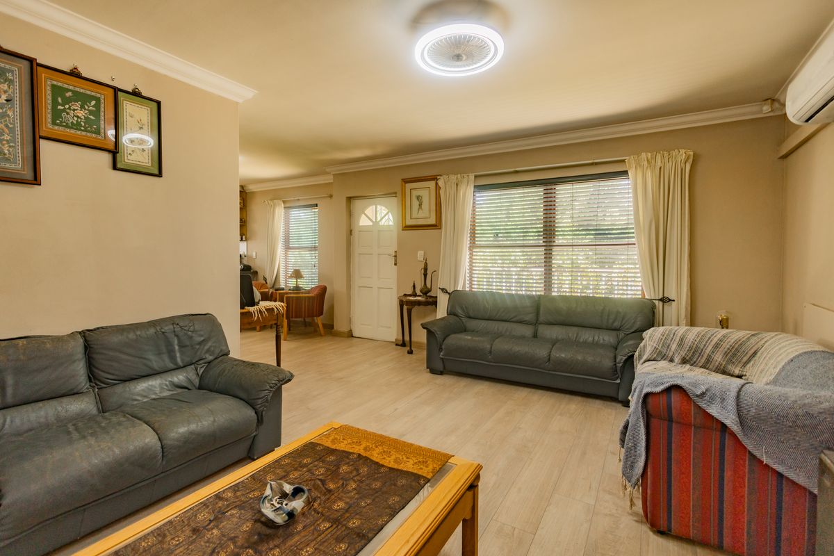 Spacious living room featuring laminate flooring, a ceiling fan, and a wall-mounted air conditioning unit, with natural light provided by large windows.