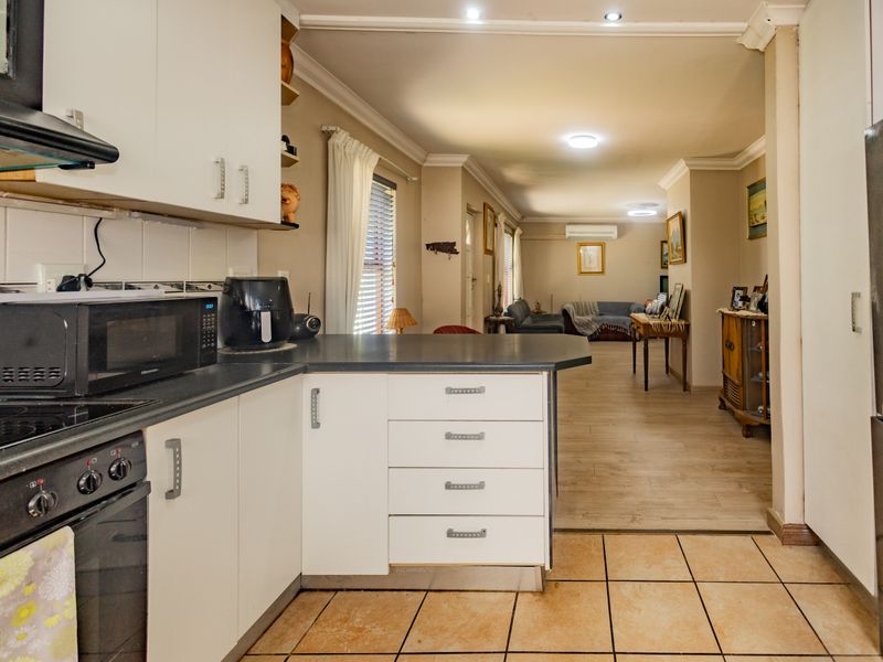 Open-plan kitchen and living area featuring white cabinetry, integrated appliances, and a combination of tiled and laminate flooring with neutral wall finishes.
