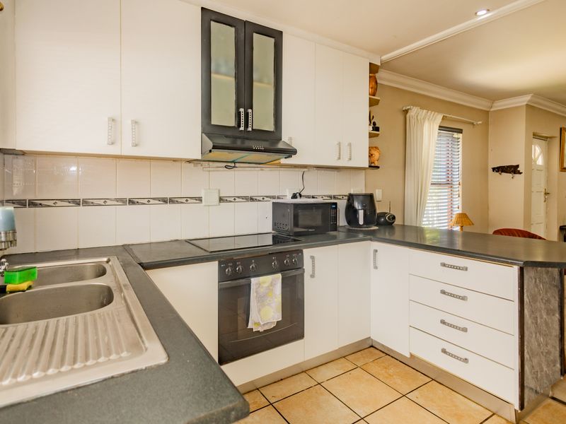 A functional kitchen featuring white cabinetry, dark laminate countertops, a built-in oven with electric cooktop, and tiled flooring.
