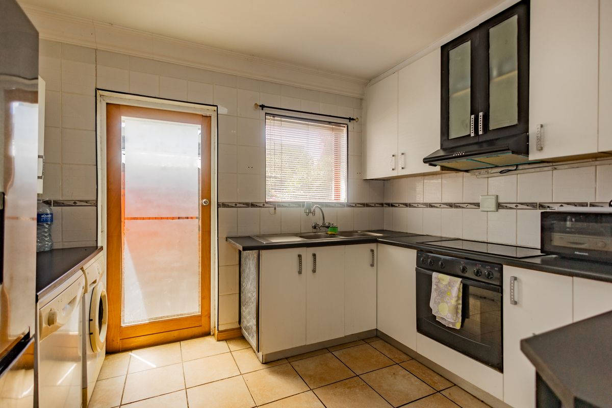 A functional kitchen featuring white cabinetry, dark countertops, built-in oven with extractor fan, tiled splashbacks, and direct access to the exterior.