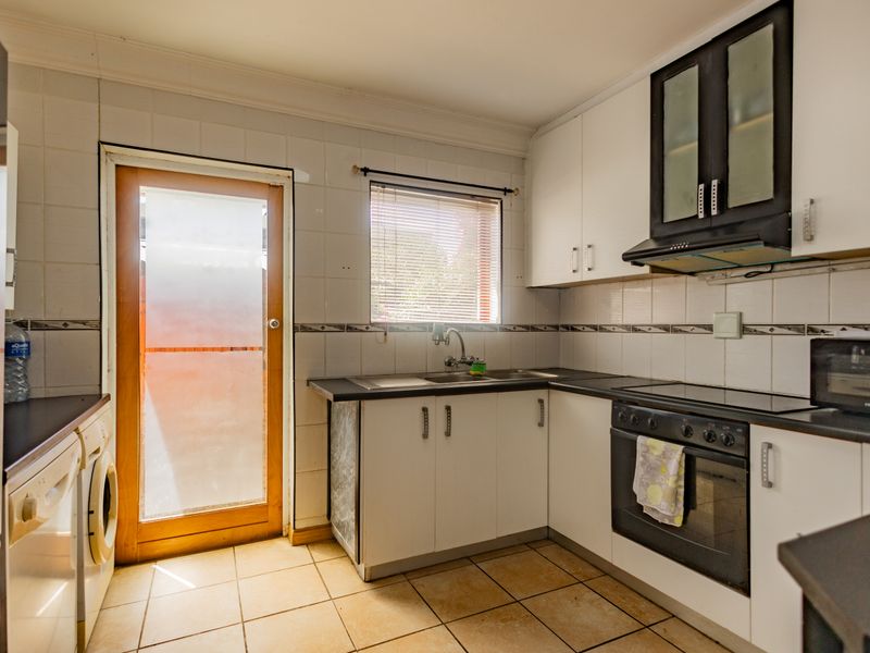 A functional kitchen featuring white cabinetry, dark countertops, built-in oven with extractor fan, tiled splashbacks, and direct access to the exterior.