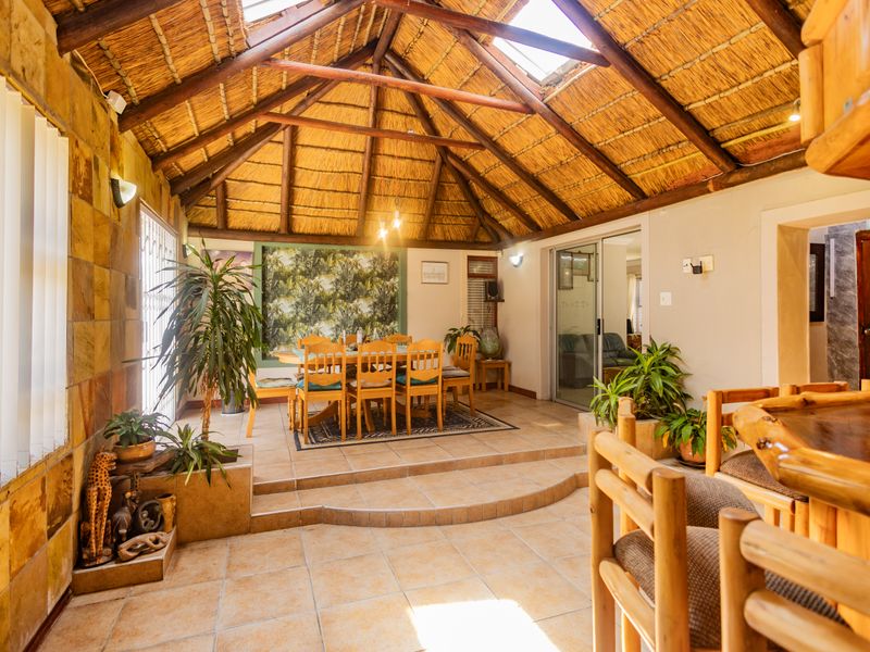 Spacious open-plan living and dining area featuring a high thatched roof with exposed timber trusses, skylights, tiled floors, and a built-in bar.