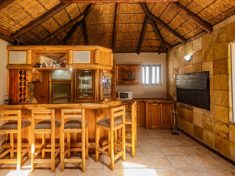 Rustic bar area featuring a traditional thatched roof, exposed timber rafters, stone wall cladding, and custom built-in timber cabinetry with a bar counter.