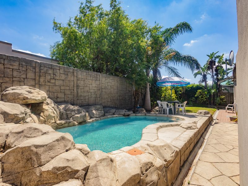 Outdoor pool area featuring a rock-scaped swimming pool, paved patio surround, and high boundary wall for privacy.