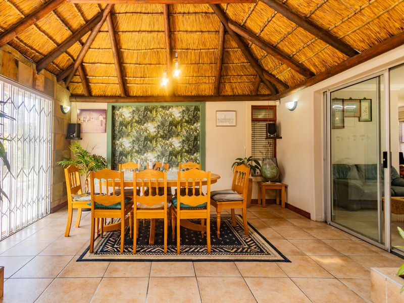 A covered patio area featuring a traditional thatched roof with exposed timber rafters, ceramic tiled flooring, and large sliding glass doors leading indoors.