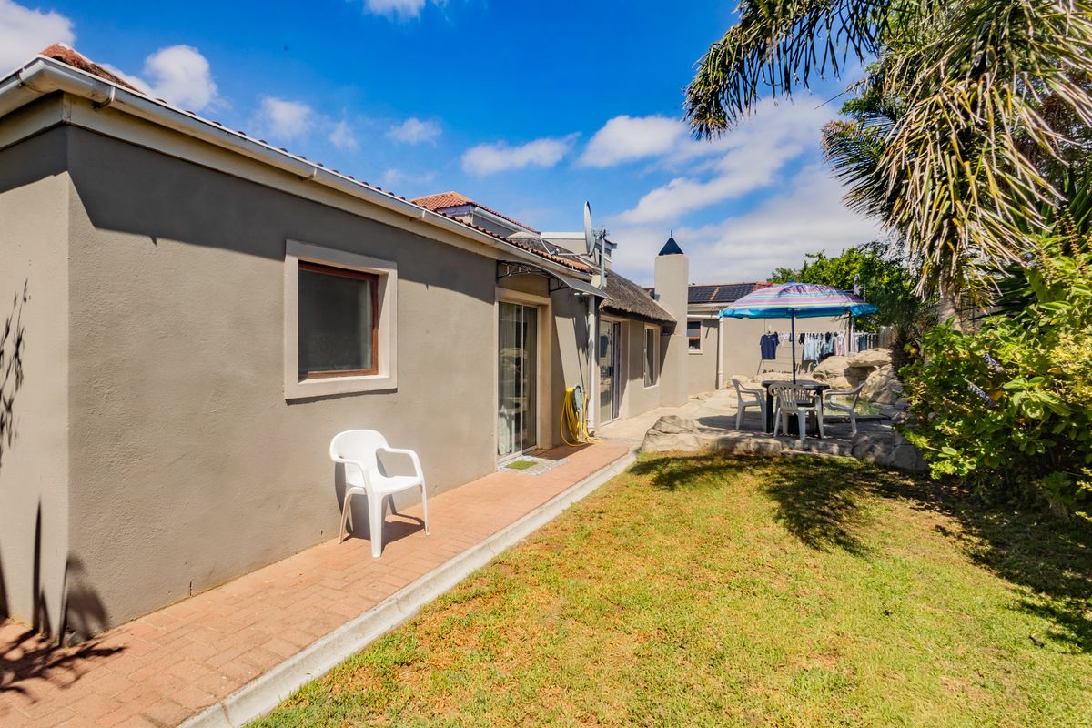 Rear exterior view of the property featuring a thatched roof, brick paved walkway, and sliding glass door access to the garden area.