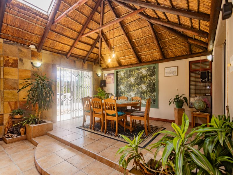 A spacious dining area featuring a high thatched roof with exposed timber rafters, a skylight, stone wall accents, and tiled flooring with a raised platform.