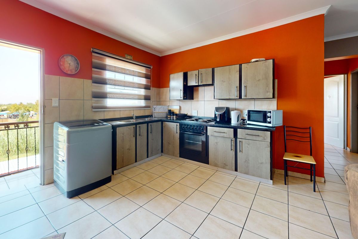 Functional kitchen featuring wood-look cabinetry, tiled backsplash, built-in oven and hob, with direct access to an outdoor balcony area.