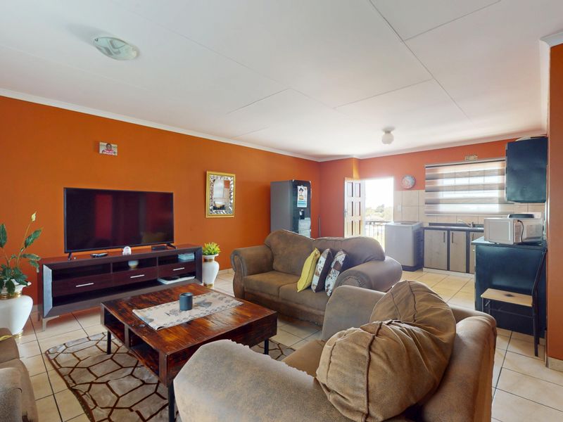 Open-plan living area featuring tiled flooring and a functional kitchen space with built-in cabinetry and sink.