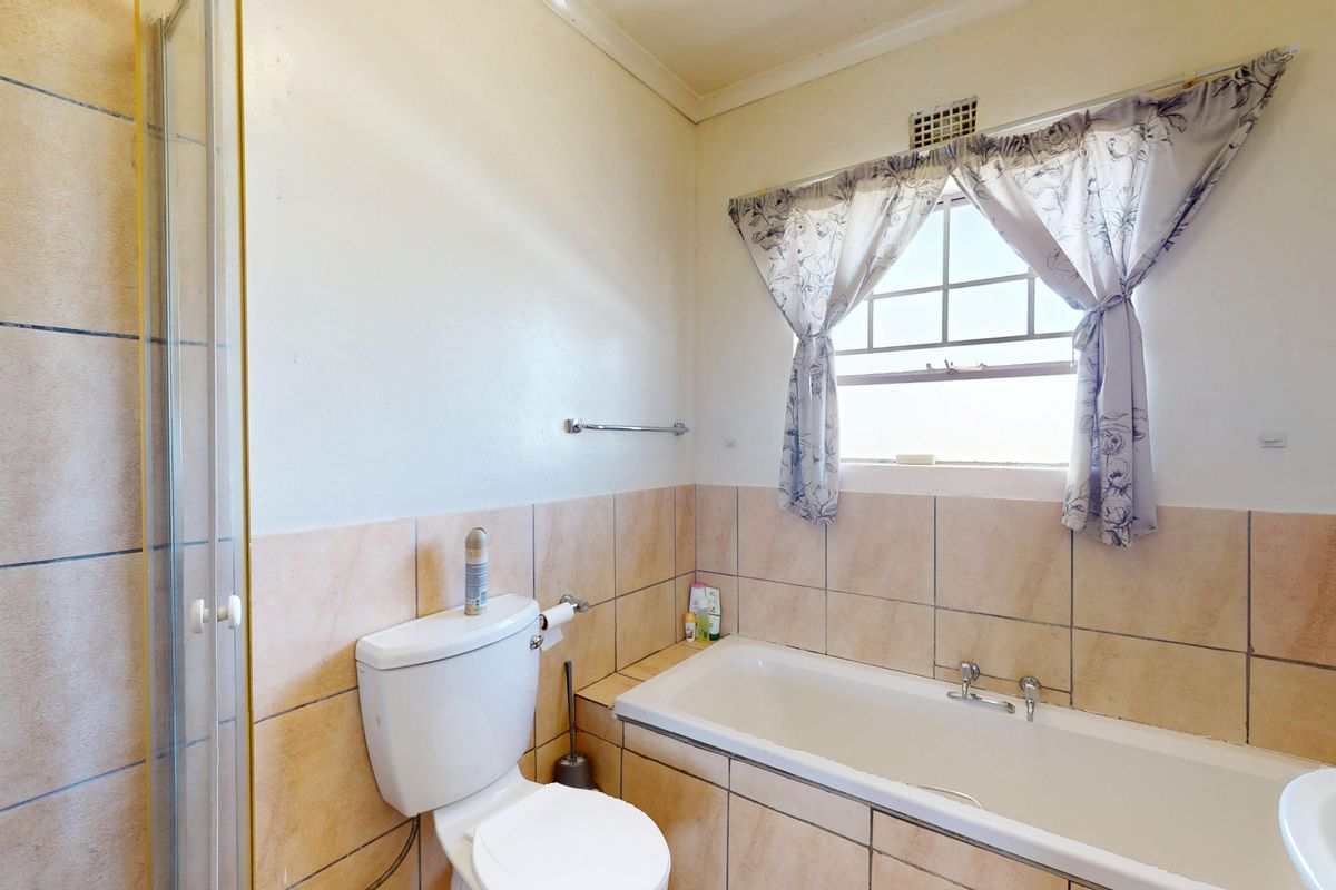 A functional bathroom featuring a bathtub, separate shower enclosure, and toilet, finished with neutral wall and floor tiling.