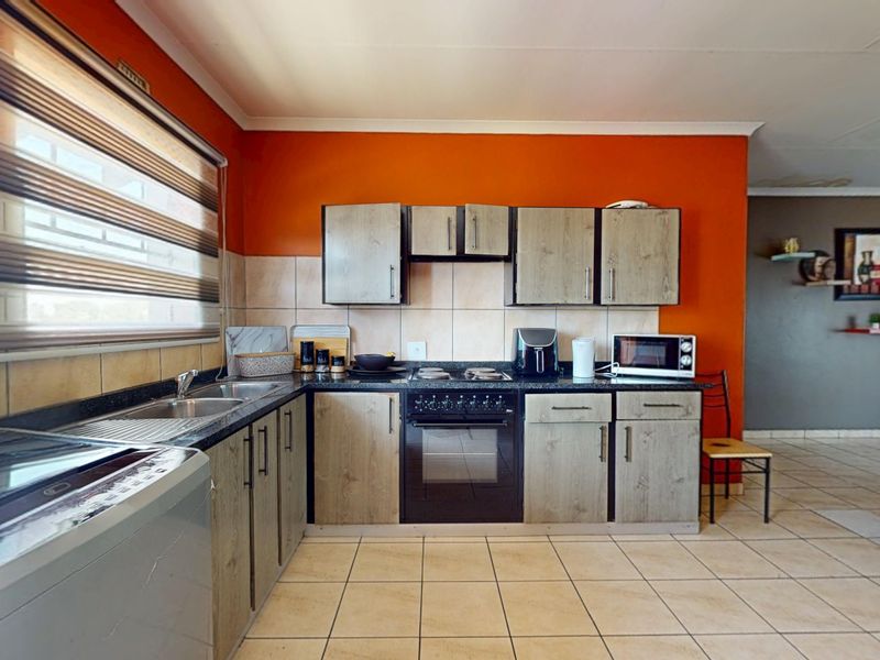 A functional kitchen featuring wood-look cabinetry, dark countertops, a built-in oven and hob, and tiled flooring with a vibrant orange accent wall.