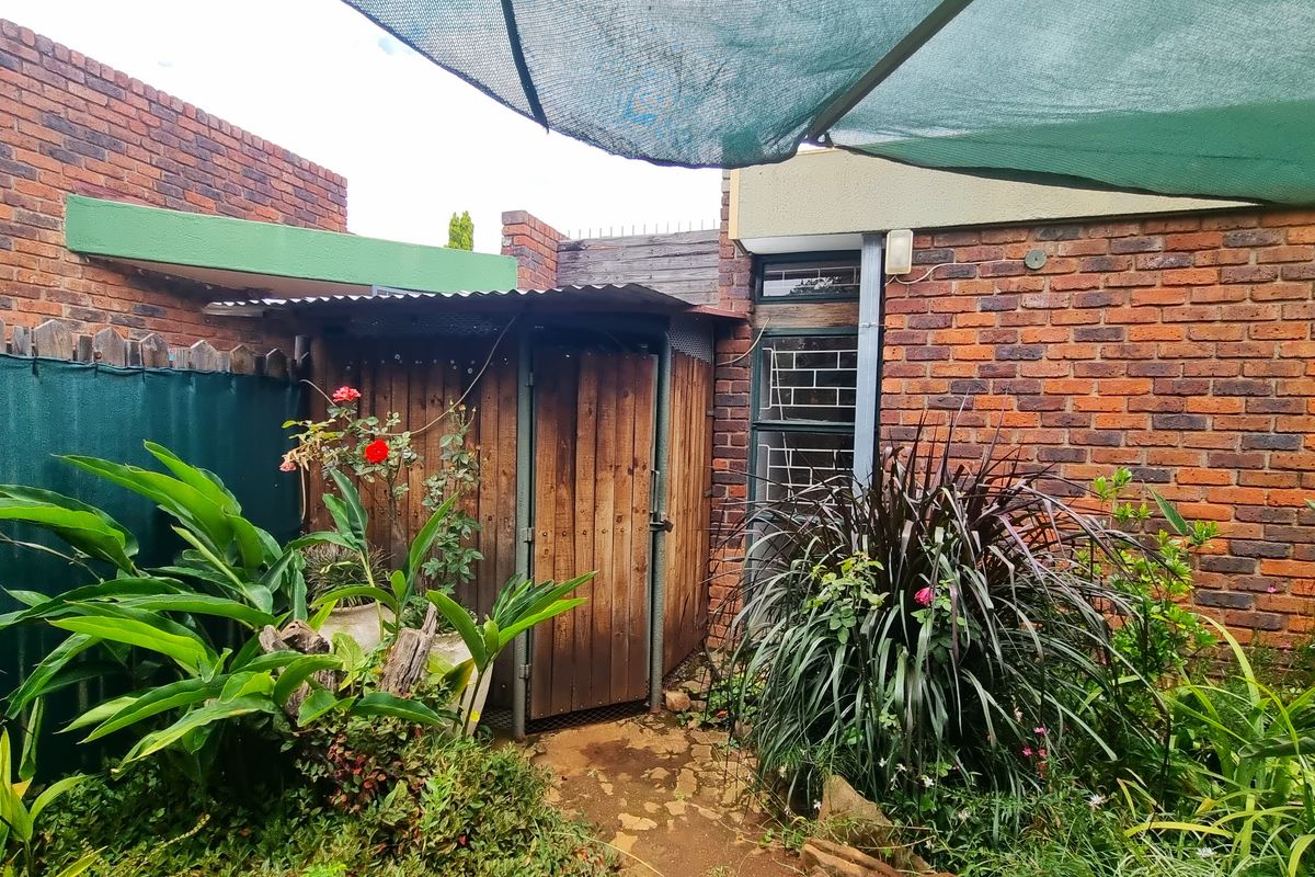 A private rear courtyard area featuring a timber storage shed, brick boundary walls, and established garden landscaping with overhead shade netting.