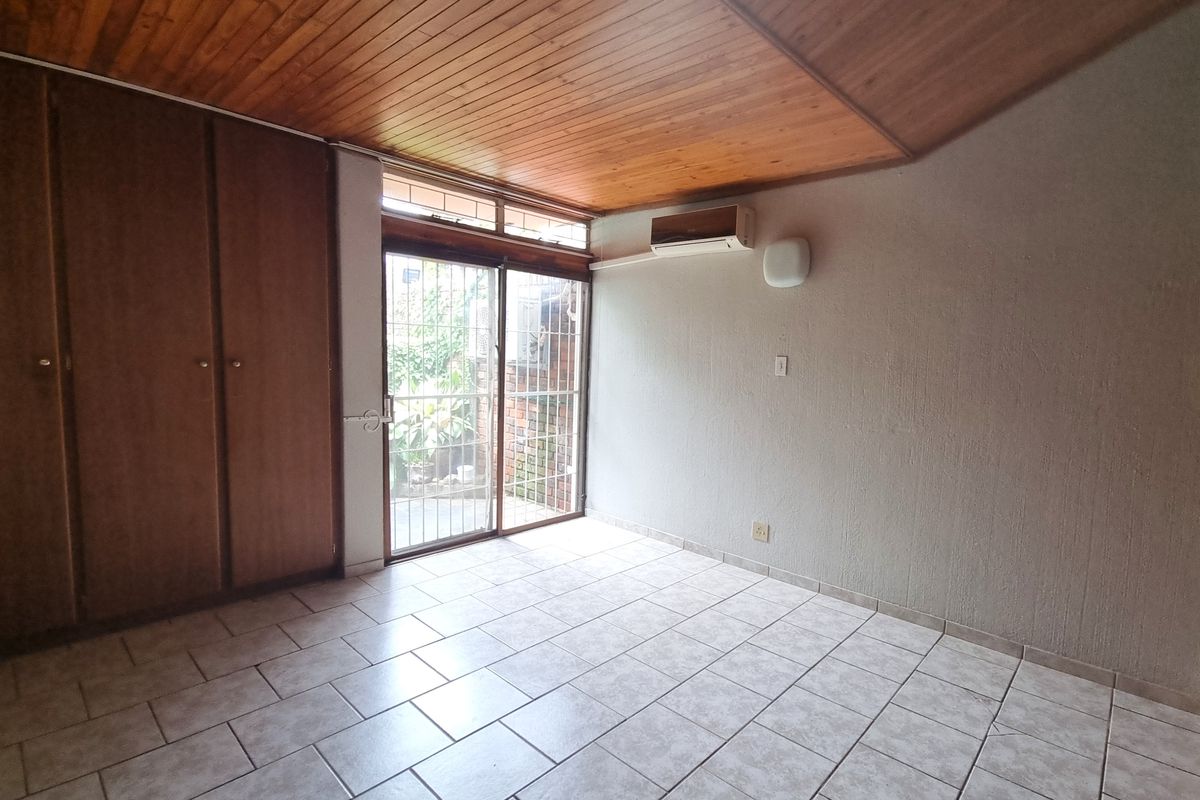 A bedroom featuring tiled flooring, built-in wooden cupboards, a timber-clad ceiling, and a sliding glass door leading to an outdoor area.