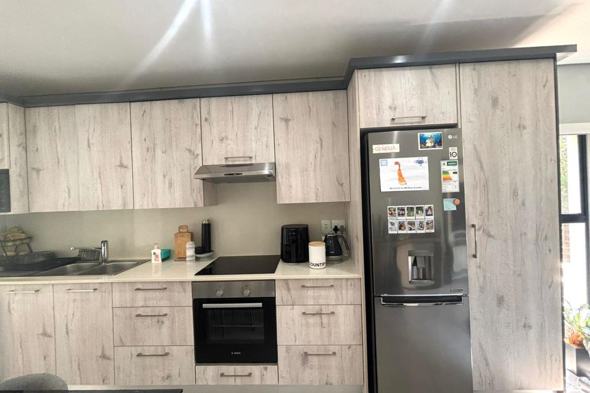 Modern kitchen featuring light wood-grain cabinetry, stone countertops, integrated oven, electric hob, and stainless steel sink with a clean, contemporary finish.