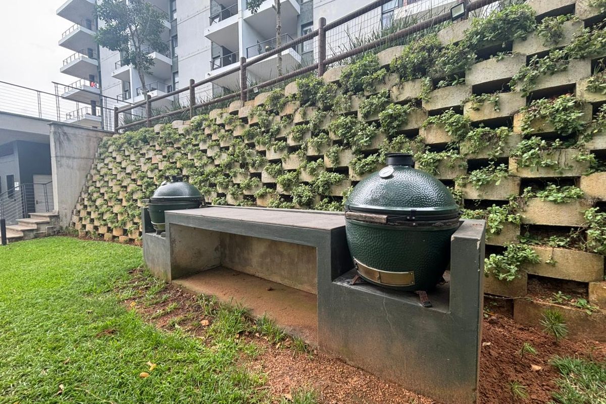 Outdoor area featuring a built-in concrete barbecue station set against a landscaped retaining wall within a residential apartment complex.