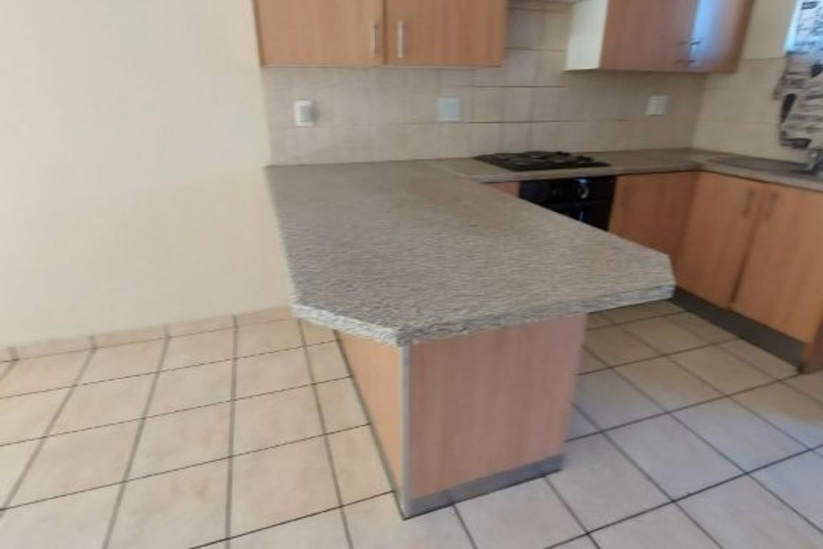 A functional kitchen featuring laminate cabinetry, a breakfast bar, built-in oven and hob, and tiled flooring throughout.